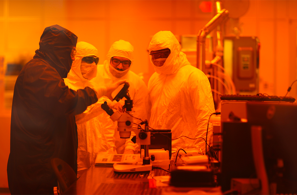 Four researchers wearing protective equipment examine a specimen in the clean room of the NC A&T and University of North Carolina Greensboro Joint School of Nanoscience and Nanoengineering building.