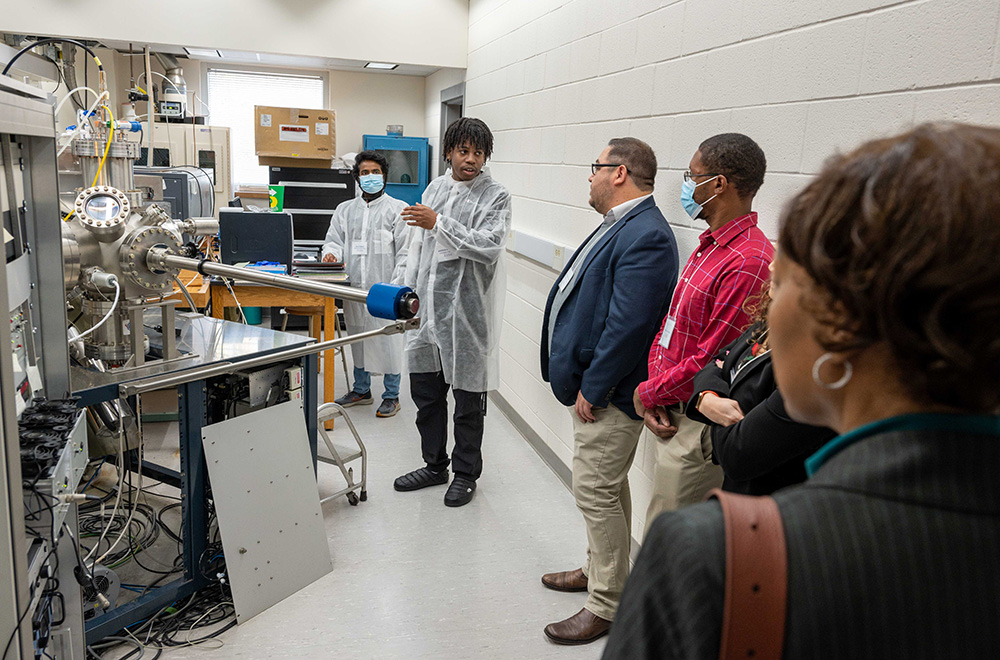 Two researchers present and explain their work to four visitors in a lab.